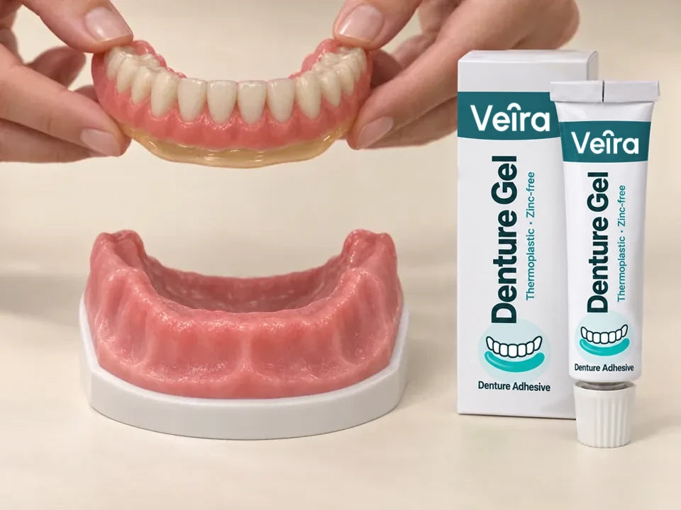 Hands hold a lower plate with a thin gel layer above a model jaw, next to a Veira Denture Gel tube and box